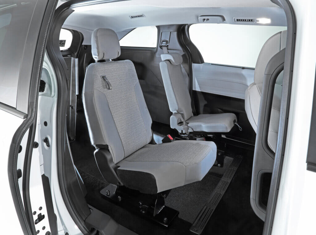 Interior view of a vehicle showing two rows of gray seats on a black floor, with ample legroom and a sliding door open on the right side.