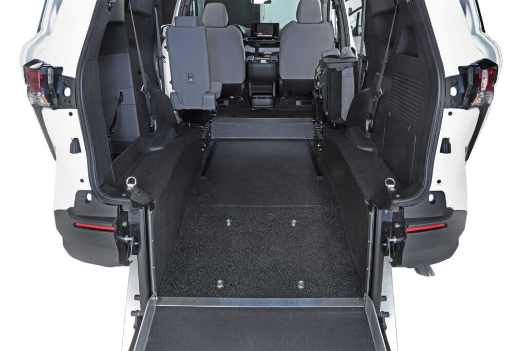 Interior view of a van with rear entry ramp, showing wheelchair-accessible space between two rows of seats and front driver/passenger seats.