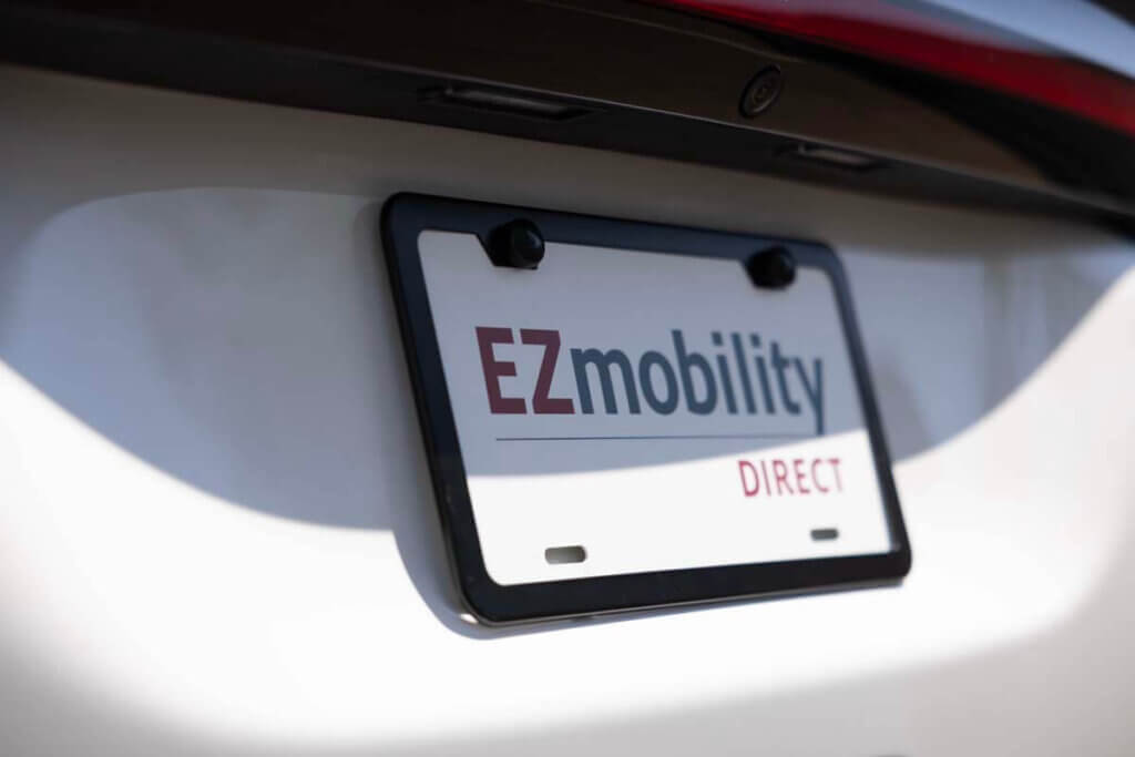 A close-up of a car license plate holder with a sign that reads EZmobility DIRECT instead of a standard license plate.